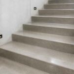 Szerokie szare schody betonowe z czarną poręczą i oświetleniem na ścianie