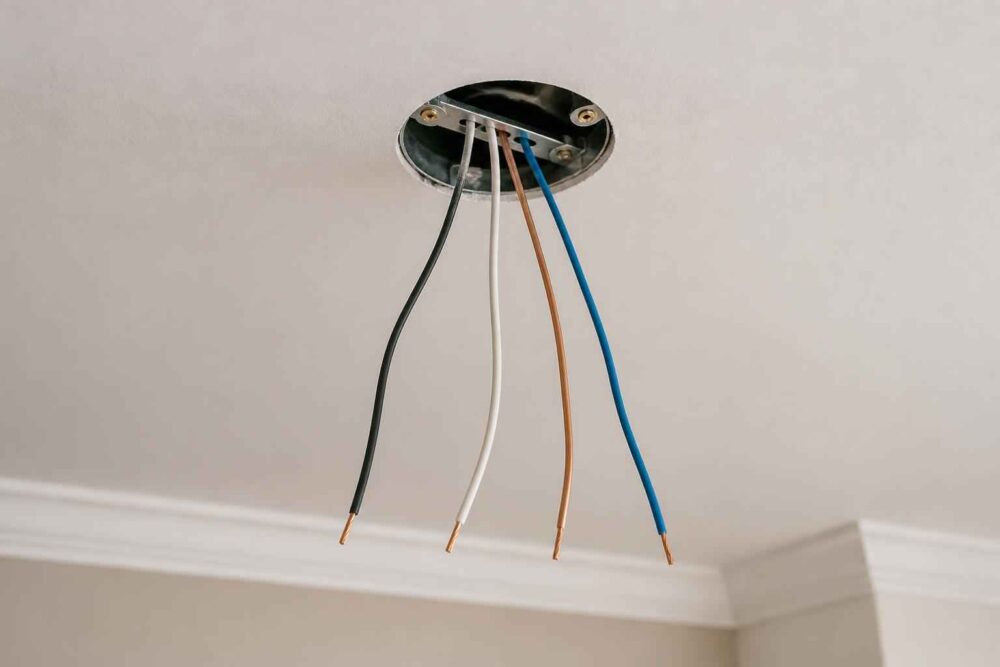 Przewody elektryczne zwisające z puszki sufitowej Kolorowe przewody elektryczne wystające z okrągłej puszki w suficie przy listwie dekoracyjnej